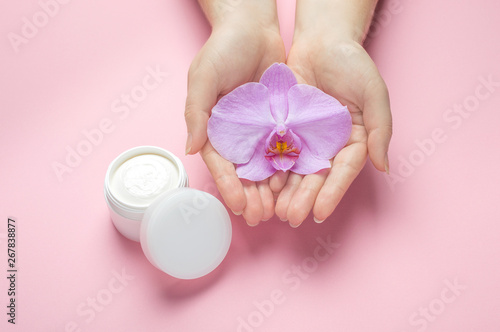 Mockup for hand skin care natural cosmetics. Woman hold orchid flower in hands on a pink background. Natural organic cosmetics with flowers extract. Beauty, fashion, cosmetology and spa concept.