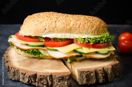 Delicious sandwiches with ham, cheese, tomatoes and salad over a wooden board on black background