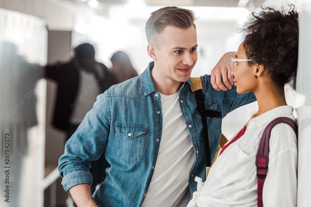 Fototapeta premium smiling multiethnic students looking at each other in corridor in university