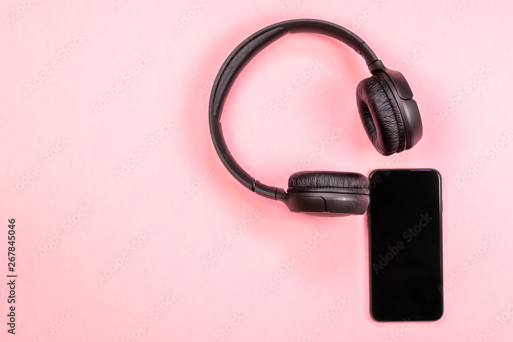 Close-up of smart phone with headphones on a pink background. (Top view). Listen to music. Close-up of smart phone with headphones on a pink background. (Top view). Listen to music.