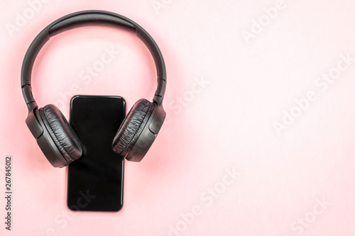 Close-up of smart phone with headphones on a pink background. (Top view). Listen to music.