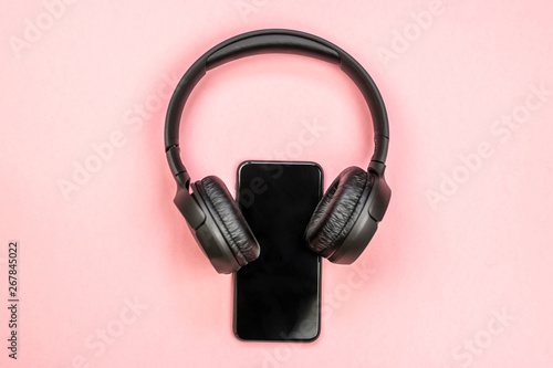 Close-up of smart phone with headphones on a pink background. (Top view). Listen to music.