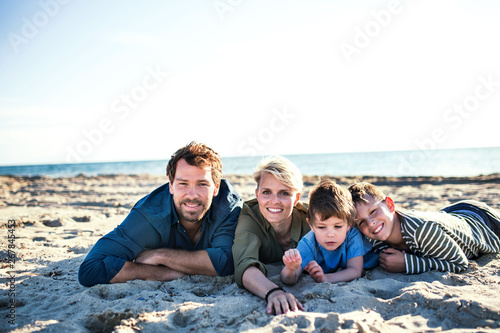 Young family with two small children lying down outdoors on beach.