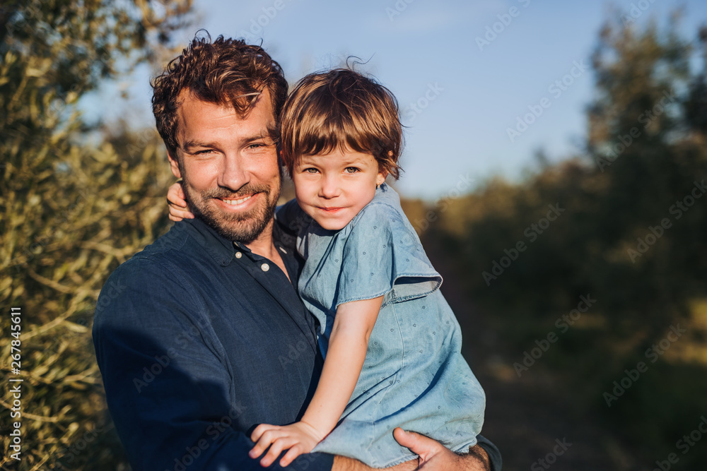 Father with small daughter standing outdoors by olive tree. Father with small daughter standing outdoors by olive tree.