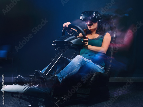 Fotografie Woman wearing VR headset having fun while driving on car racing simulator cockpit with seat and wheel
