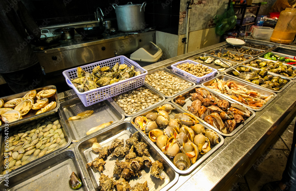 Street food at night in Hanoi, Vietnam. Delicious seafood for tourist at street market. Fresh shells and musles open kitchen. Traditional asian dishes.