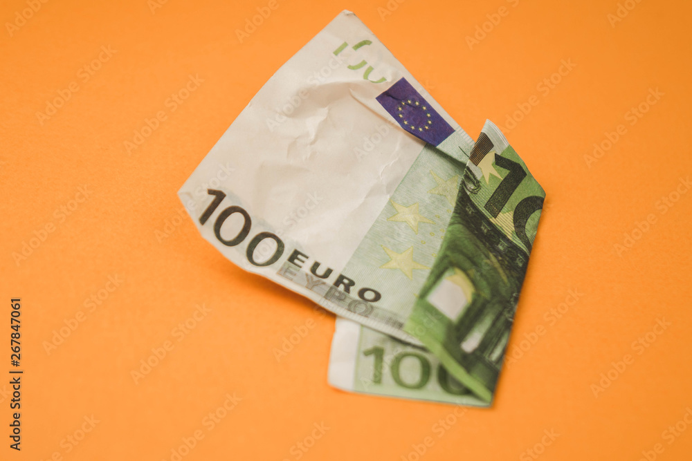 Obraz premium zmięte sto euro leżącego na pomarańczowym tle