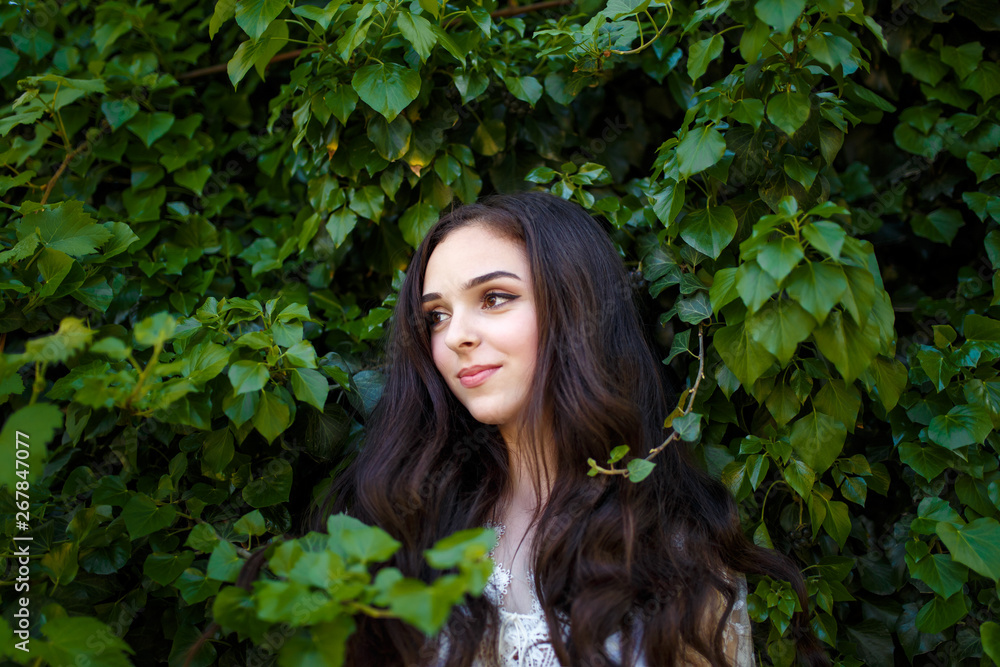 young teenager girl portrait with long dark wavy hair standing on the green ivy background young teenager girl portrait with long dark wavy hair standing on the green ivy background