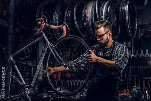 Handsome serious man in protective glasses is fixing bicycle at his own shop.