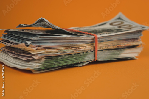 bundle of dollars lying on orange background close up