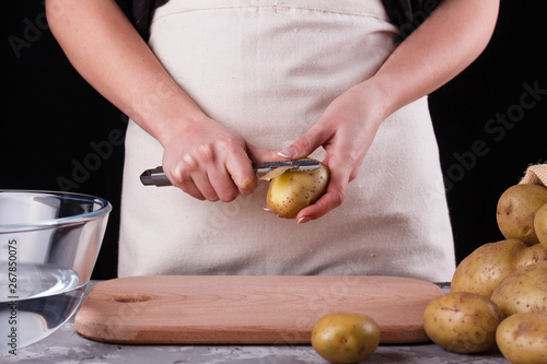 A young woman in an apron peeling potatoes