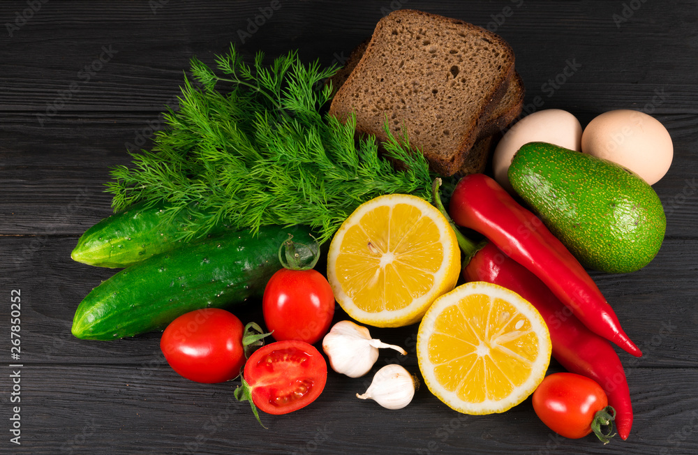 .Healthy food-tomatoes, cucumbers, avocados, bread, greens, onions, garlic, eggs, chili pepper on a black background