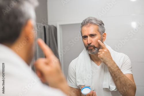 middle aged man putting face cream in bathroom