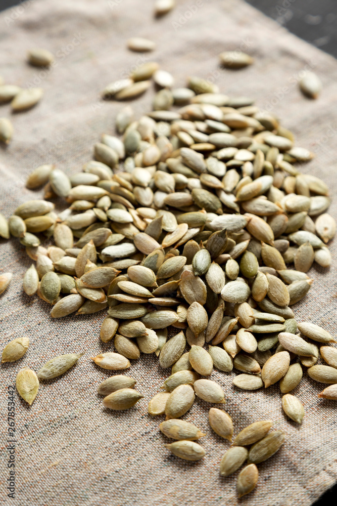 Fototapeta premium Roasted pumpkin seeds on cloth over black surface, side view. Close-up.