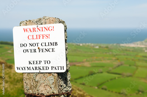 Sign warning walkers not to climb over fence due to danger of high cliffs