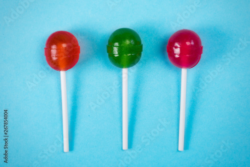 Three lollipops on a stick, at the white pastel background, the view from above.