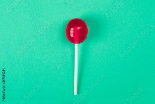 Tablou pe pânză A red lollipop on a stick at the green background, a view from above, sweets and caramel