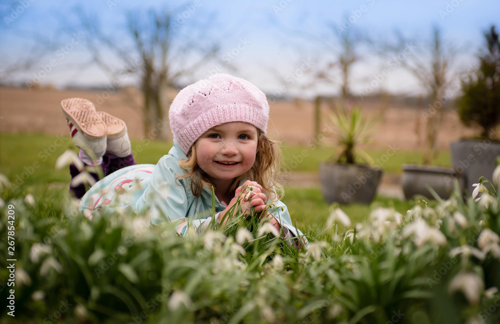 Little girl in hat lying beside snowdrops smiling Little girl in hat lying beside snowdrops smiling