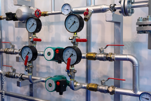 Heating system's pipes with ball valves and manometer on a grey wall