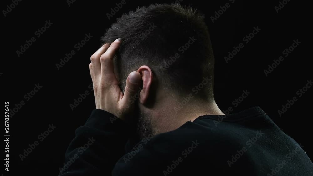Hopeless man closing face with hands and deeply crying against dark background Hopeless man closing face with hands and deeply crying against dark background