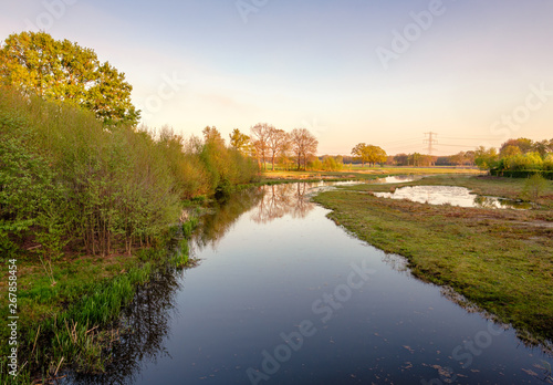 Calm river along a walking trail in a Dutch farm landscape during sunset. It is located near the small neighbourhood called Tusveld, near the town of Almelo in the Eastern Netherlands.