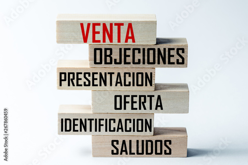 A list of wooden blocks lying on top of each other with a list of sales techniques in Spanish, in the translation of the word: sale, objections, presentation, sentence, identification, greeting