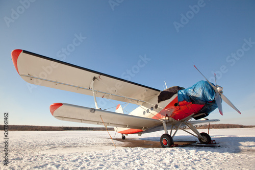 Fototapeta Naklejka Na Ścianę i Meble -  Soviet light multipurpose aircraft used as an agricultural, sports, transport, passenger aircraft,  stored in winter in the territory of a private airfield. Blue sky and frost weather. Light biplane