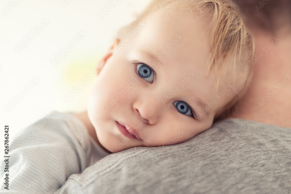 Close-up portrait of cute adorable blond caucasian toddler boy on fathers shoulder indoors. Sweet little child feeling safety on daddys hand. Responsibility and childcare. happy childhood Close-up portrait of cute adorable blond caucasian toddler boy on fathers shoulder indoors. Sweet little child feeling safety on daddys hand. Responsibility and childcare. happy childhood