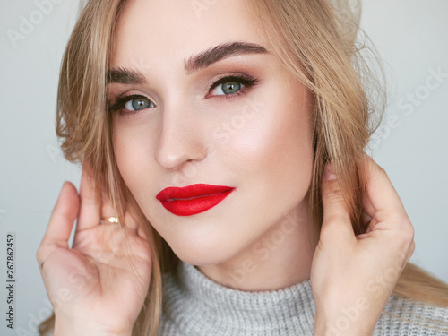 Closeup natural light beauty portrait of blonde woman model with vibrant saturated red lips bright lips makeup, cheekbones and healthy shiny skin.