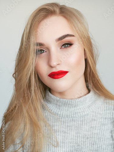 Closeup natural light beauty portrait of blonde woman model with vibrant saturated red lips bright lips makeup, cheekbones and healthy shiny skin.