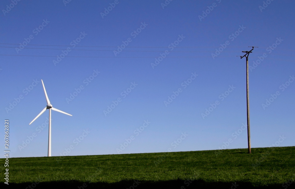 Fototapeta premium Wind turbine and power line on a field against the blue sky