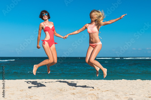 Two young attractive women are jumping on the beach and having fun during vacation on Bali island.