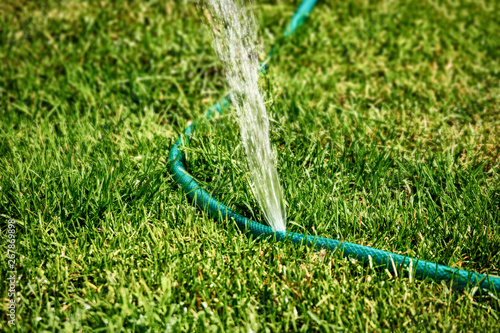 DIY lawn sprinkler working in grass spreading water all over the area, copyspace