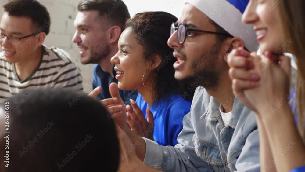 Diverse young people sitting in front of TV in flat, watching sport game and feeling down because of team's fail Diverse young people sitting in front of TV in flat, watching sport game and feeling down because of team's fail