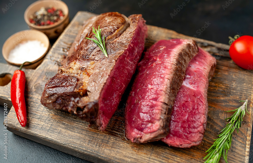 Grilled rib eye beef steak with herbs and spices on a stone background