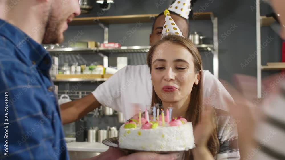 Caucasian birthday woman blowing out candles on cake while friends doing circle dance around her Caucasian birthday woman blowing out candles on cake while friends doing circle dance around her