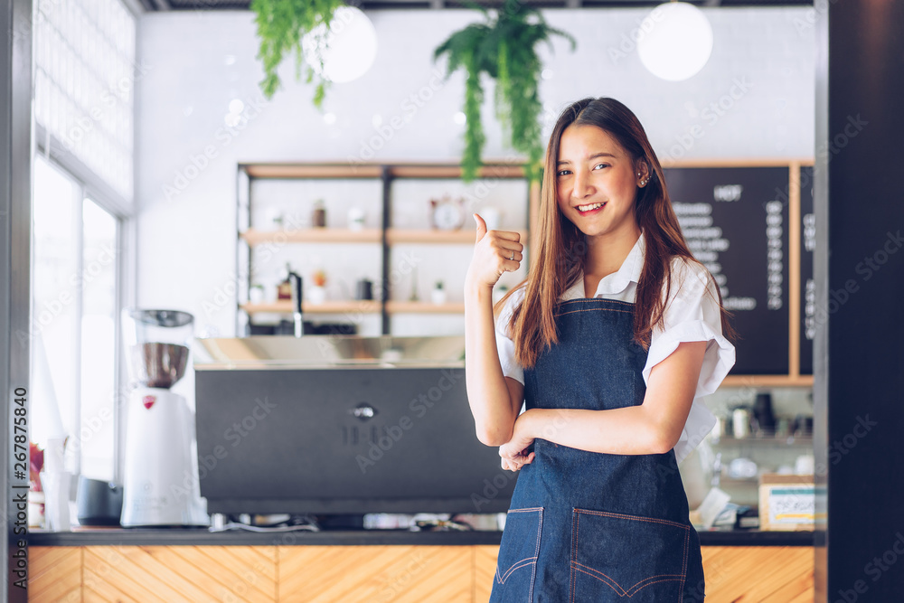 Pretty young asian waitress standing arms crossed in cafeteria.Coffee Business owner Concept. barista in apron smiling at camera in coffee shop counter Pretty young asian waitress standing arms crossed in cafeteria.Coffee Business owner Concept. barista in apron smiling at camera in coffee shop counter