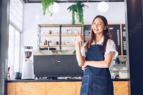 Pretty young asian waitress standing arms crossed in cafeteria.Coffee Business owner Concept. barista in apron smiling at camera in coffee shop counter