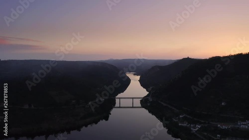 Beautiful bridge reflection on the river, between silhouette mountains. Wide shot by drone at sunset with an amazing and dramatic orange and purple sky. Portas de Rodão, Portugal photo
