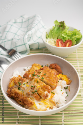 Close up rice bowl topped with deep-fried pork cutlet and eggs decorated with salad in Japanese style