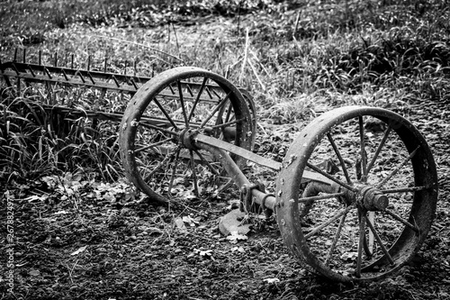 Black and white old farm equipment wheels in a field.
