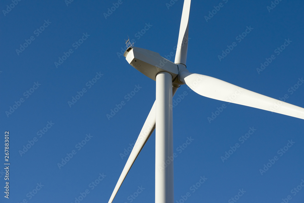 Close up of a wind farm turbine against a clear blue sky.