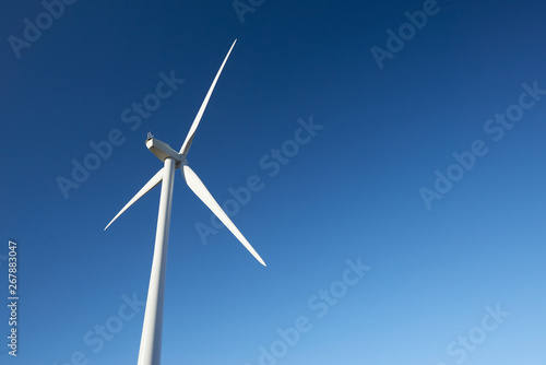 Close up of a single turbine from behind on a wind farm against a clear blue sky. © Chris Mirek Freeman