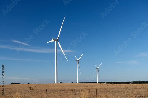 Three wind turbines on a farm in an Australian landscape.