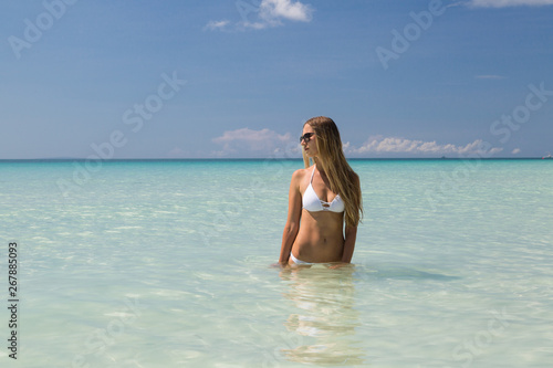 Sexy tanned girl in white swimsuit posing on the sea. Beautiful model sunbathes and rests on ocean shore. Concept vacation  travel  swimwear