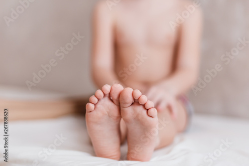 the child is sitting barefoot on the bed, children bare little feet
