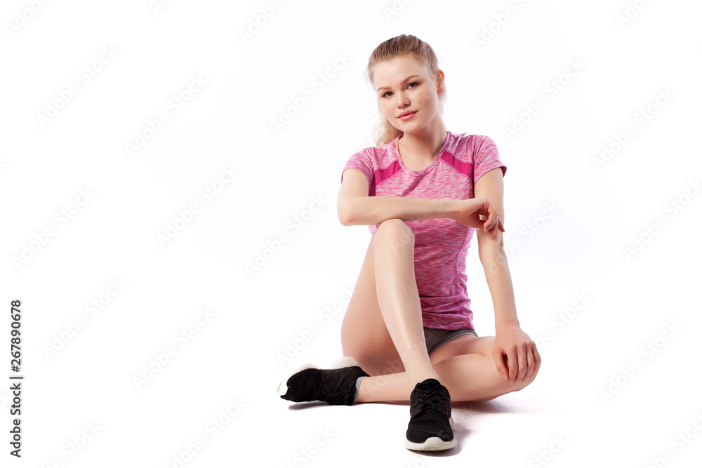 Young woman in sports clothes smilling, possing and sitting on the floor on white isolated background. Side view.Fit girl living an active lifestyle Young woman in sports clothes smilling, possing and sitting on the floor on white isolated background. Side view.Fit girl living an active lifestyle
