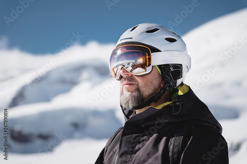 Close-up athlete skier in helmet and ski mask against the snow-capped mountains of a ski resort with a reflection of the Caucasian mountains in the mask © yanik88