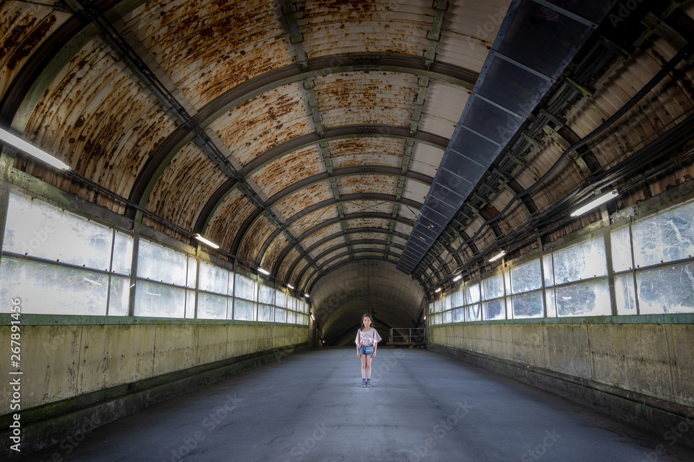 Young girl stands center of old train station walkway 