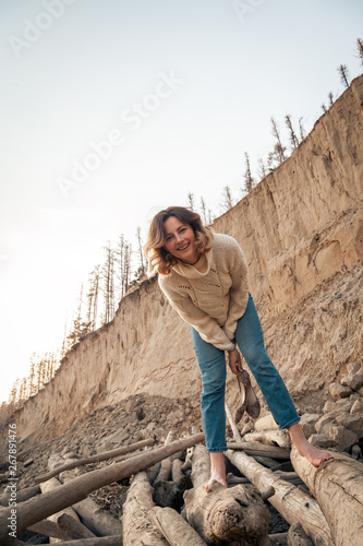 Outdoor atmospheric lifestyle photo of young beautiful darkhaired woman white knit sweater made of natural wool and jeans in on the beach, in the background the sea with sunset.